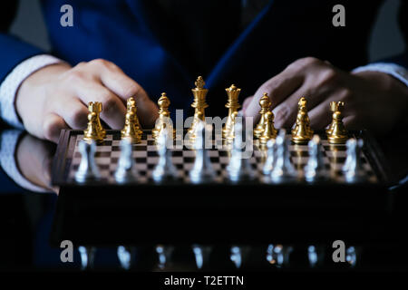 Immagine ritagliata di imprenditore in tuta di pensare sul movimento mentre è seduto al tavolo di vetro e giocare a scacchi Foto Stock