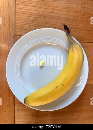 Banana e pillola, integratori alimentari su una piastra bianca, marrone tavolo in legno, Germania Foto Stock
