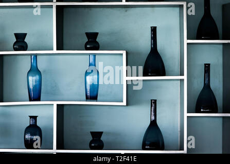 In stile retrò blu bottiglie di vetro in una bellissima disposizione sugli scaffali attaccato ad una luce blu parete. Foto Stock