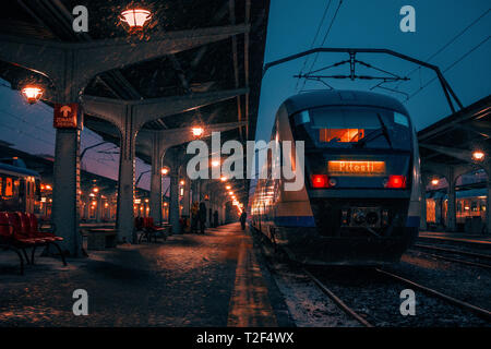 Gli esseri umani nel buio su di una stazione ferroviaria sulla piattaforma durante una tempesta di neve e un treno nella stazione sulle vie di Bucarest Nord Railway Foto Stock