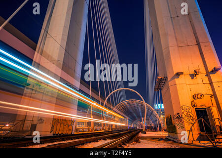 Night Shot con esposizione lunga con una fermata del tram che passa da e lasciare striature chiare e due rotaie utilizzato dal tram per il trasporto pubblico che passa su un mod Foto Stock