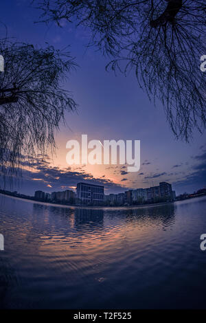 Mattina cityscape di scena a sunrise in primavera con un edificio residenziale che riflette nell'acqua e alcune nuvole in background Foto Stock