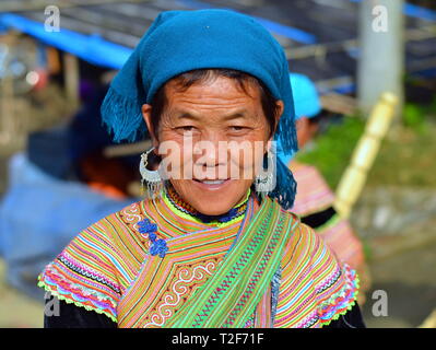 Anziani fiore vietnamita H'mongs donna indossa il costume tradizionale del fiore H'mongs persone, un velo di colore blu e grandi orecchini in argento. Foto Stock