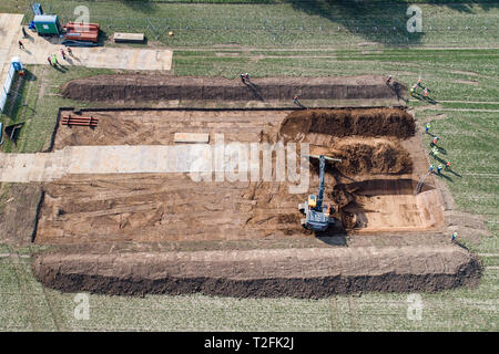 02 aprile 2019, Bassa Sassonia, Göttingen: Un escavatore scava un campo di prova di circa 2500 metri quadrati sulla prova Reinshof farm. Gli effetti della metropolitana linee di potenza sul terreno lungo la prevista linea elettrica ad alta tensione sono Wahle-Mecklar per essere simulato sulla superficie a nome della griglia operatore Tennet e studiato da scienziati agricoli presso l'Università di Göttingen. (Foto aeree con drone) Foto: Swen Pförtner/dpa Foto Stock