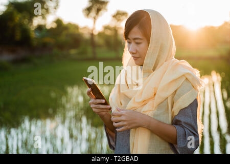 Donna musulmana con il hijab utilizzando il telefono cellulare per esterno Foto Stock