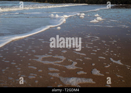 Spuma bianca schiuma di cucitura lavaggio fino sulla spiaggia la sera Sun, in Broadstairs Kent Foto Stock