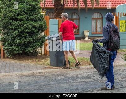 Johannesburg, Sud Africa - senzatetto non identificato uomo attende per un proprietario di abitazione non identificato il cassonetto in ordine alla ricerca di cibo o di oggetti riutilizzabili Foto Stock
