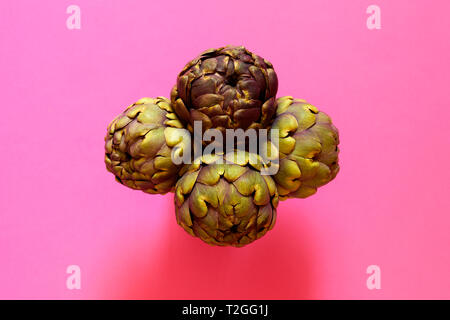 Gruppo di 4 carciofi isolato dal di sopra su un sfondo fucsia flatlay concept Foto Stock