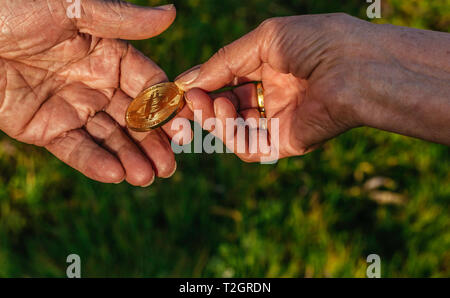 Senior donna mano è azienda moneta bitcoin dando ai senior man mano sulla natura verde dello sfondo. Economia, finanza, investimenti e lo scambio di nozioni Foto Stock