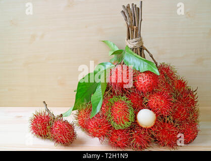 Grappolo di colore rosso e verde fresco Rambutan maturi frutti interi e pelati isolato su un tavolo di legno Foto Stock