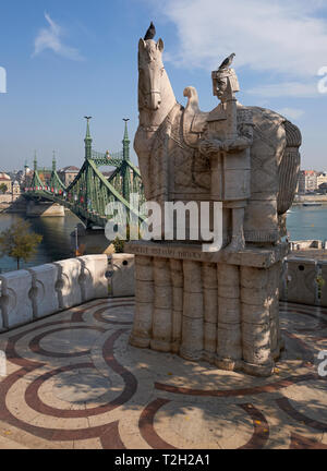 Statua di Santo Stefano al di fuori della Chiesa Grotta, Colle Gellert Budapest, Ungheria, con il ponte della Libertà in background. Foto Stock