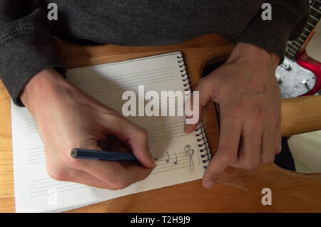 Giovane uomo comporre musica in un notebook personale collocato sul retro di una chitarra. Musicista iscritto nello studio di musica. La composizione in chiave di violino. Foto Stock