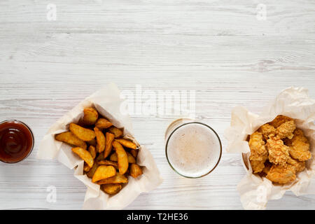 Bocconcini di pollo, Spicchi di patate un bicchiere di birra fredda e salsa barbecue bianco su una superficie di legno, vista dall'alto. Copia dello spazio. Foto Stock