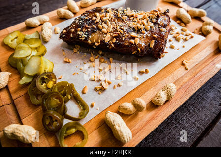 Primo piano di costolette di maiale alla griglia con salsa barbecue serviti con arachidi e jalapeno. Messa a fuoco selettiva Foto Stock