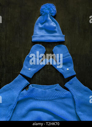 Tappo con pompon, muffole, maglione in blu-viola-colore ciano sul legno scuro dello sfondo. Vista superiore, piatto lay.Concetto gioventù elegante caldo autunno-inverno. Foto Stock