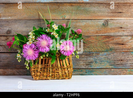 Bouquet di fiori di trifoglio, cornflowers e gelsomino nella Cesta in vimini bianco sul tavolo di legno sul retro grunge sfondo con spazio di copia Foto Stock