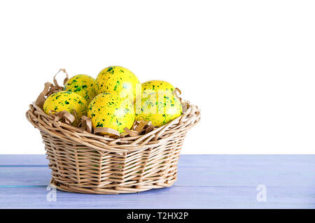 Giallo di Pasqua le uova in un cesto di paglia. Blu su sfondo di legno. Isolare bianco. Sfondo vuoto. Foto Stock