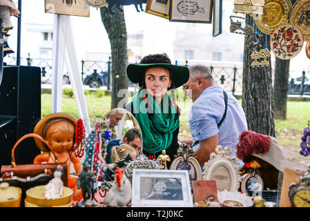 La Russia, città Mosca - 6 Settembre 2014: giovane bella ragazza in un cappello con riproduzione e sciarpa verde. Una donna che vende oggetti di antiquariato in un mercato di strada Foto Stock