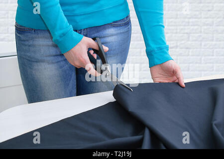 Ragazza caucasica tagli di panno nero sul tavolo. In camera. Close-up. Foto Stock