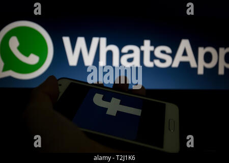 Logo di Facebook è mostrato su un display dello smartphone, WhatsApp non focalizzato il logo su sfondo Foto Stock