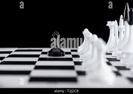 Messa a fuoco selettiva di scacchiera bianca con pezzi di scacchi e pedone nero davanti isolato su nero Foto Stock