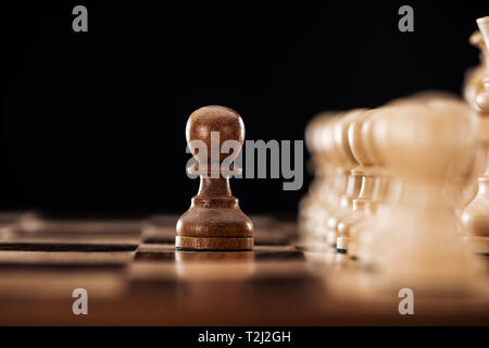 Messa a fuoco selettiva di scacchiera in legno con pezzi di scacchi e pegno di fronte isolato su nero Foto Stock