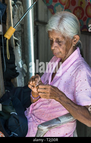 Galle, Sri Lanka - Febbraio 18th, 2019: Ritratto di una donna senior di infilaggio di un ago seduti all'aperto del suo workshop a Galle, Sri Lanka. Foto Stock