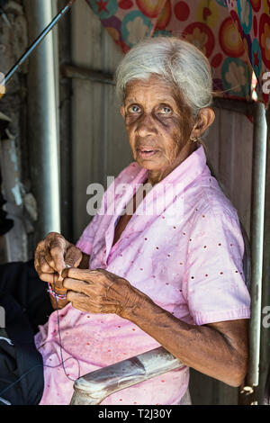 Galle, Sri Lanka - Febbraio 18th, 2019: Ritratto di una donna senior di infilaggio di un ago seduti all'aperto del suo workshop a Galle, Sri Lanka. Foto Stock