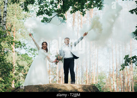 La sposa e lo sposo stand su una scogliera e tenere premuto fumo bombe nelle loro mani in bianco. Foto Stock