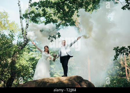 La sposa e lo sposo stand su una scogliera e tenere premuto fumo bombe nelle loro mani in bianco. Foto Stock