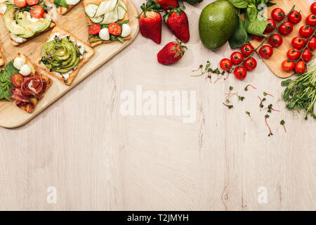 Vista superiore del pane tostato con verdure e prosciutto sul tavolo di legno con ingredienti Foto Stock