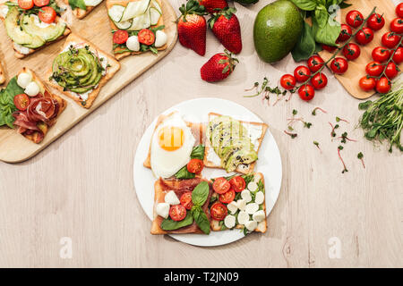 Vista superiore degli ingredienti e toast con verdure, uova fritte e prosciutto sul tavolo di legno Foto Stock