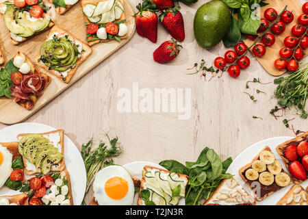 Vista superiore del pane tostato con verdure e frutta e il prosciutto con il verde e gli ingredienti sul tavolo di legno Foto Stock