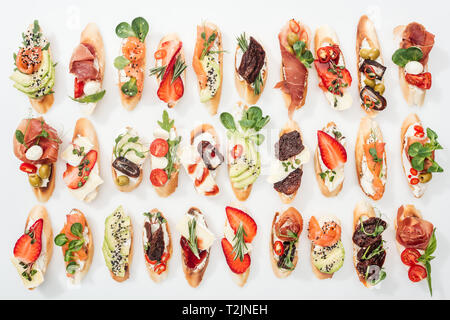 Sfondo di deliziose bruschette con salmone, prosciutto, pomodori secchi, avocado, le fragole e le erbe su bianco Foto Stock