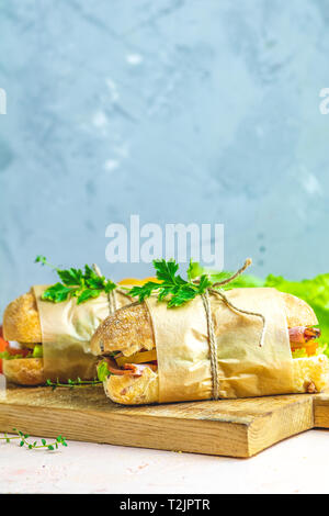 La ciabatta in sandwich con prosciutto e pomodoro, formaggio, pepe, cipolla e insalata sul tagliere di legno con ingredienti. Foto Stock