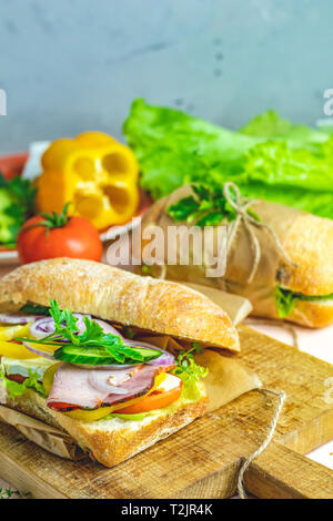 La porchetta italiana sandwich. La ciabatta in sandwich con prosciutto e pomodoro, formaggio, pepe, cipolla e insalata sul tagliere di legno con ingredienti. Foto Stock