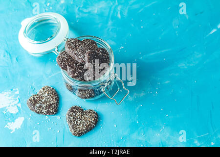 Deliziosa cotta al cioccolato a forma di cuore i biscotti con scaglie di noce di cocco in un barattolo di vetro sul calcestruzzo blu la superficie del tavolo. Cibo biglietto di auguri con copia spazio per Foto Stock