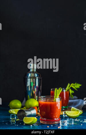 I succhi di pomodoro con sedano, spezie, sale e ghiaccio nella porzione bicchieri con copia spazio. Bloody Mary cocktail. Le bevande alcoliche e gli ingredienti al buio Foto Stock