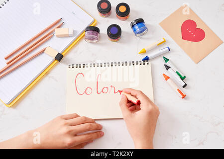 Mano con matite di colore e il foglio di carta sul tavolo bianco Foto Stock