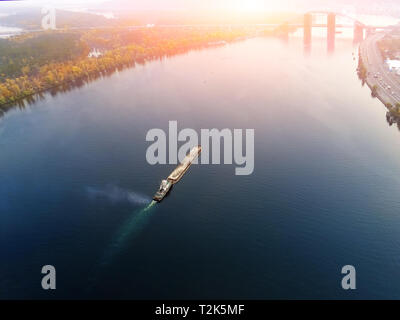 Scenic aerial cityscape di Kiev e il fiume Dnipro al tramonto. Rimorchiatore chiatta di supporto con sabbia di materiali alla rinfusa voce lungo il fiume Dnieper. In Ucraina Foto Stock