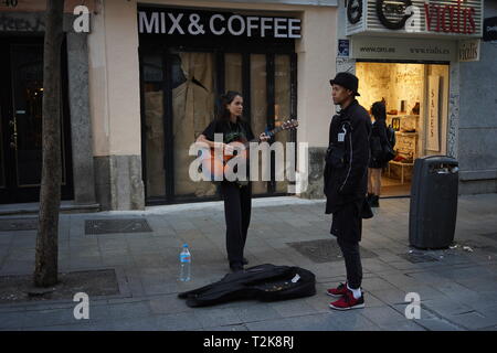 Artista di strada che suona la chitarra con un amico con cappello in una zona pedonale di Madrid, Spagna Foto Stock