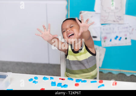 Ispanico giovane ragazzo che esprimono o dirompente comportamento disordinato in una classe con lettere dell'alfabeto manipulatives sulla scrivania. Foto Stock