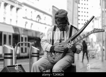 Suonatore ambulante di strada suonando la chitarra con una maschera a gas su Foto Stock