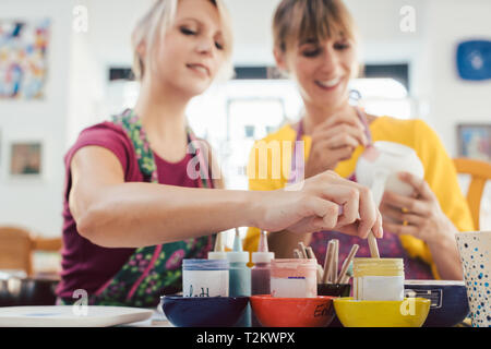 Due amiche dipinto loro ceramiche fatte a mano in un workshop hobby Foto Stock