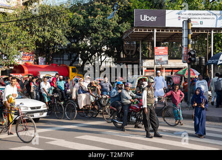 " Commuter " sono visti in attesa ad un semaforo accanto a un annuncio per American online ride-la condivisione e la rete di trasporti società Uber di Dhaka. Foto Stock