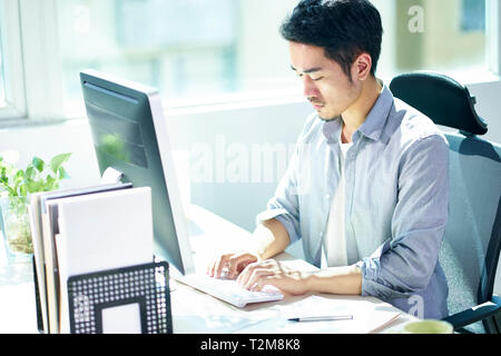Elevato angolo di visione di un giovane imprenditore asiatici imprenditore lavora in ufficio con computer desktop. Foto Stock