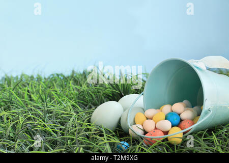 Colore naturale uova Easeter e malto candy uova fuoriuscita da un robin blu uovo cestello di metallo in erba con camera per copiare lo spazio. Foto Stock