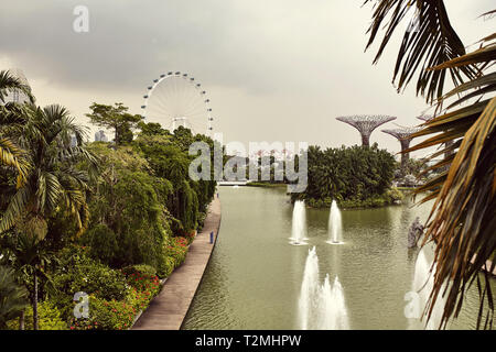 Parco presso i giardini dalla baia circondata da alberi con una vista di una ruota panoramica Ferris in distanza. Foto Stock