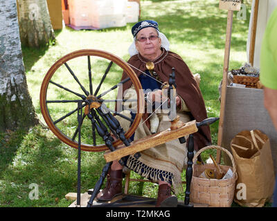 Hämeenlinna, Finlandia - Agosto 17, 2014: donna anziana creazione sbadiglio con una vecchia ruota di filatura al festival medievale su una soleggiata giornata estiva. Foto Stock