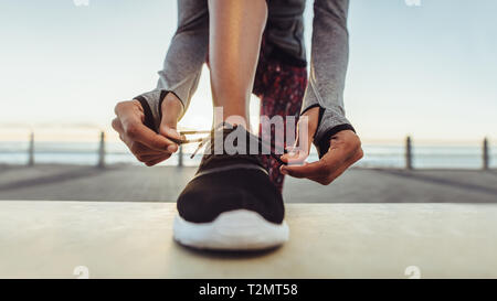 La donna la sua legatura lacci prima di correre. Runner la sua legatura lacci delle scarpe mentre la formazione outdoor su una strada dal mare. Foto Stock